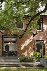 Modern house exterior made of brick with visible interior space through an open door, surrounded by greenery.