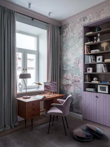 A contemporary home office with a desk, chair, bookshelf, and floral wallpaper.