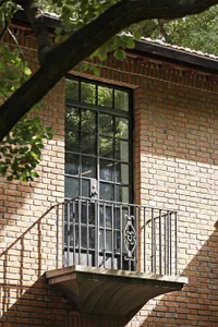 A section of a brick building exterior featuring a classic black metal door and balcony with wrought iron railings.