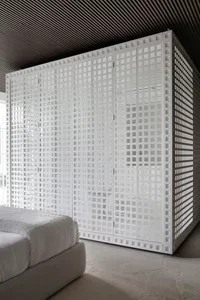 A minimalist bedroom with a white, textured plaster wall, featuring a bed with white bedding and a white, geometrically patte