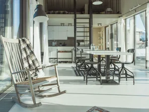 A minimalist residential interior featuring wood and metal furniture, a glass table, and white walls.