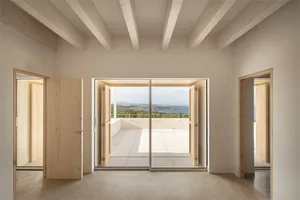 A minimalist residential space with wooden doors and a concrete floor, offering a view of the ocean.