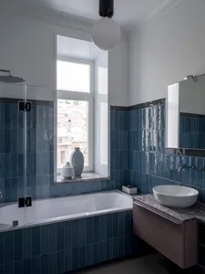 Modern bathroom with blue tiles, bathtub, sink, and window with natural light.