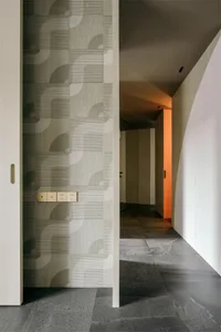 A modern corridor features a tiled floor with a textured, abstract design, and a white wall with a light switch.