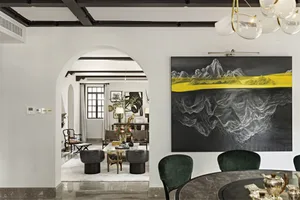A modern dining room with a round marble table, green velvet chairs, and a large abstract art piece featuring yellow and blac