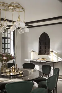 A modern dining room with a round marble table, green velvet chairs, and glass tableware.
