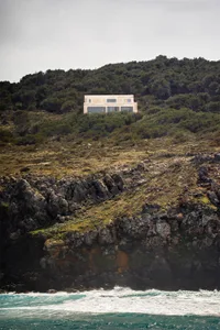 A modern house built on a cliff overlooking the ocean.