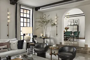 Modern living room with marble and glass decor, featuring a grey sofa, black chairs, and a glass table.