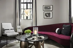A modern living room featuring a dark, curved velvet sofa with marble accents, a marble coffee table, and a white armchair un