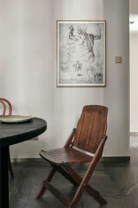 A modern living room with a wooden folding chair, a round wooden table, and an art piece depicting human anatomy hanging on t