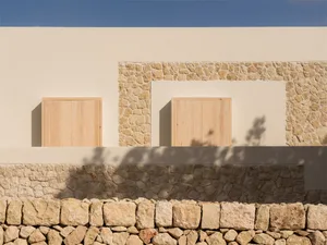 Modern minimalist exterior featuring wooden shutters and stone walls under a clear blue sky.