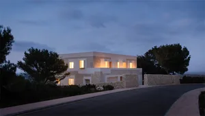 A modern white stone concrete residential home with lights on during dusk.