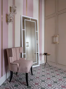 A room with pink-striped walls, a patterned floor tile, and a tall white-framed mirror.