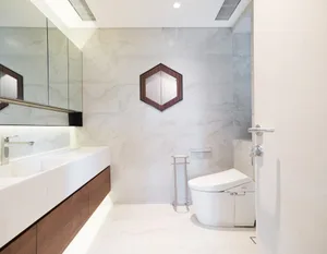 A modern bathroom featuring marble walls and floor tiles, a white toilet, and a wooden vanity with a single sink.