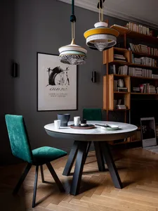 Minimalist living room with wood flooring, a round table with a glass top, green cushioned chairs, and a bookshelf filled wit