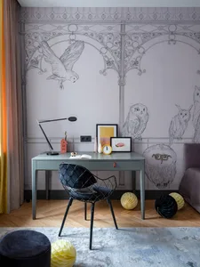 A modern home office with a grey desk, black chair, and a wall decorated with intricate grey owl sketches.