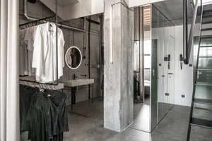 Modern minimalist clothing storage area with concrete walls, glass doors, and metal railings.