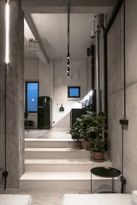 A minimalist interior designed with concrete materials, featuring a sleek black fridge and greenery.