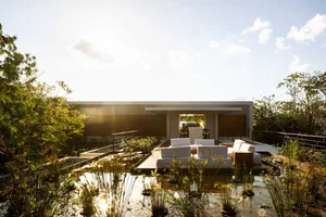 A minimalist roof garden featuring wood furniture, concrete structure, glass elements, and lush green plants.