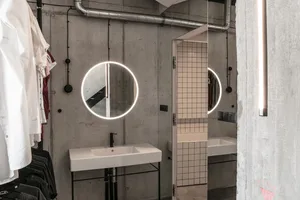 Modern bathroom featuring exposed concrete walls, glass shower, and circular light fixture.