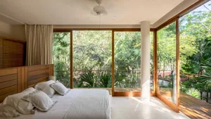 A modern bedroom featuring a white bed and a large window overlooking lush greenery.