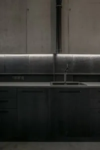 Modern kitchen with minimalist design featuring black metal cabinets and a tiled backsplash.