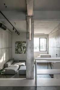 Modern, minimalist living room with concrete walls, a gray sectional sofa, and a hanging linear light fixture.