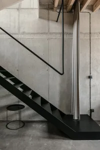 Modern industrial staircase with black metal railing and concrete steps against a raw concrete wall.