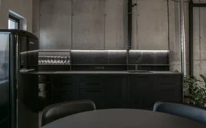 A modern kitchen with metal cabinets, black countertops, and a black refrigerator.