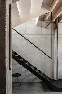 Modern minimalist interior featuring black stairs, concrete walls, and a black table.