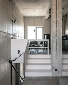 A modern, minimalist living space with concrete walls and floors, featuring a staircase leading to an upper level.