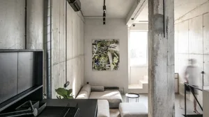Modern minimalist living room with concrete walls and a grey sectional sofa.