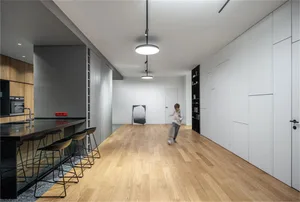 Person running through a minimalist living room with wooden flooring, white walls, and a kitchen island with black countertop