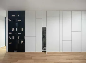 A minimalist bedroom with white paneling, black shelving, and a hidden storage compartment.
