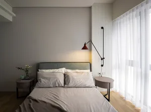 A minimalist bedroom with a bed, side tables, and a wall-mounted lamp.