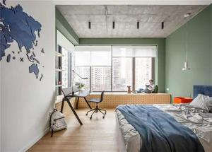 A minimalist bedroom with a concrete ceiling, wooden floor, and a green wall. There is a bed with blue bedding, a desk area, 