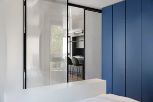 Modern, minimalist bedroom with glass walls and blue storage cabinets.