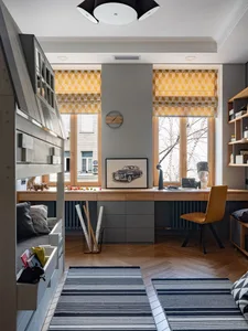 Minimalist home office with a wooden desk, yellow geometric window shades, and a grey and white striped rug.