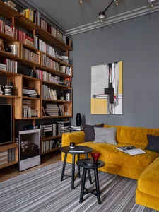 A minimalist living room with a bright yellow couch, wooden shelves, and a gray rug.