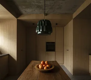 A minimalist residential kitchen featuring wooden cabinets and a wooden dining table with a bowl of oranges.