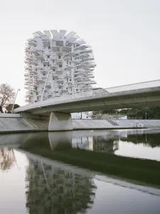 Concrete building with geometric balconies reflected in calm river waters, modern architectural style.