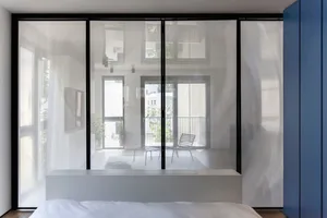 A modern bedroom featuring a large glass wall that provides a view of the outside and allows natural light to flood the space
