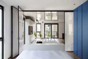 Modern minimalist bedroom with white walls, glass walls, and wood flooring.