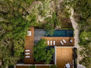 Aerial view of a modern residential home with a wooden boardwalk and swimming pool surrounded by trees.