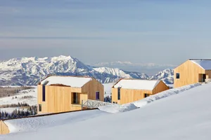 Modern, minimalist homes covered in snow with mountainous background.