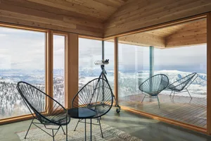 A minimalist living room with large glass windows overlooking a snowy landscape.