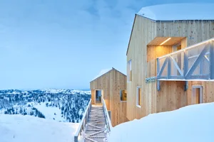 Modern ski lodge exterior with wooden and metallic elements, featuring a snow-covered landscape.