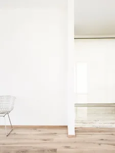 A minimalist room with wooden flooring and a metal wire chair against a white wall.