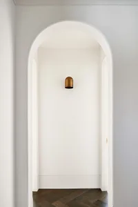 A modern minimalist interior with a white arched doorway and a wooden floor.