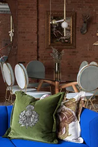 A cozy dining area with green velvet pillows, glass tables, and a brick wall, celebrating industrial design aesthetics.